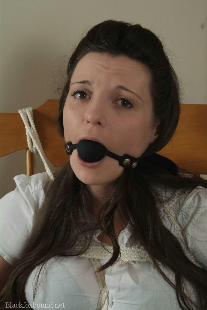 Dark haired girl has her tits exposed while ballgagged and tied up